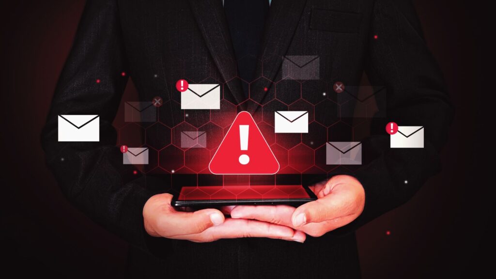 Dłonie trzymają telefon nad którym są symbole wiadomości i wykrzyknik - symbol phishingu w mailu.